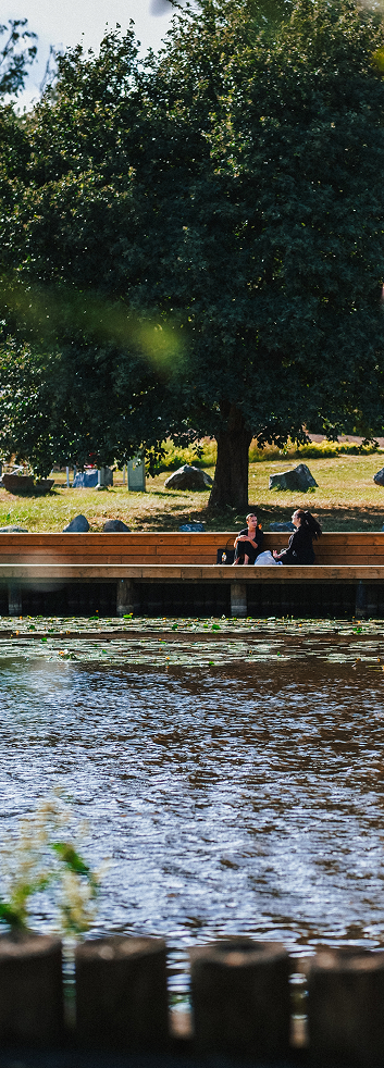 Two people sitting on bench by river